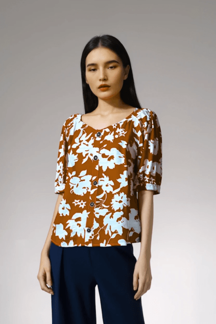 Blusa con estampado floral blanco sobre fondo naranja lúcuma, con mangas abullonadas y botones frontales.